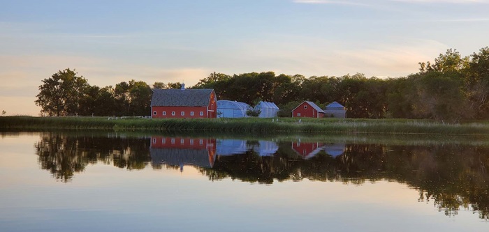Farm buildings reflecting against a lake at sunset 
